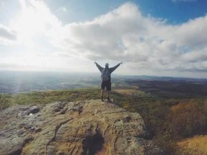 man with arms raised on top of a mountain